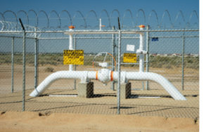 High pressure gas pipeline access point enclosed in a fence topped with razor wire.